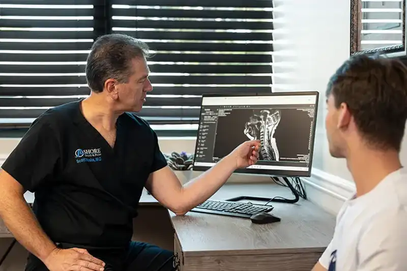 A physician points to lumbar X-ray imaging on a tablet during a spondylolisthesis evaluation at Shore Spine & Pain in NJ.