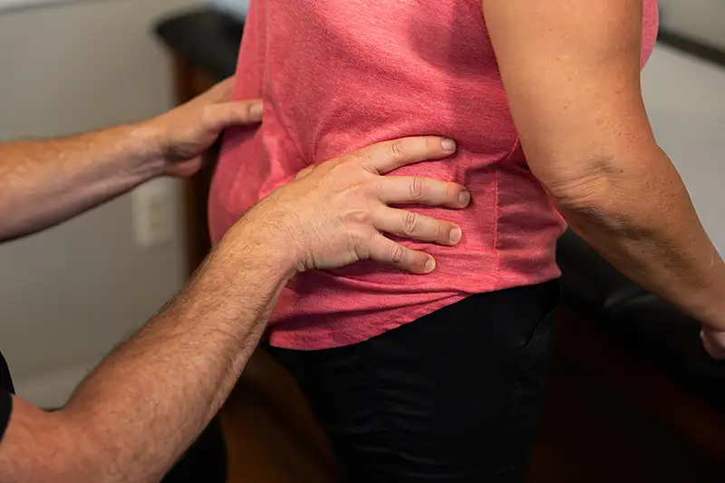 A woman grips her lower back with a digital skeletal overlay showing sacroiliac joint pain treated at Shore Spine & Pain.